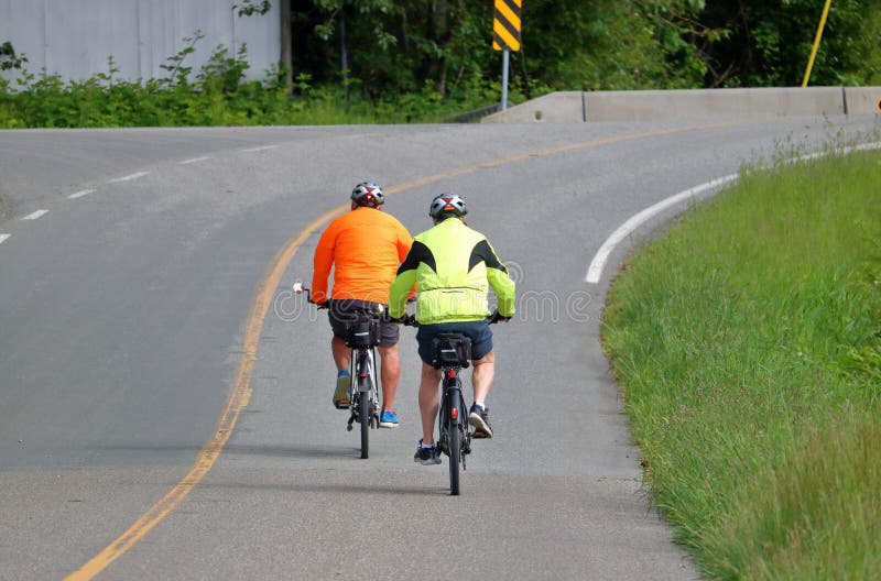 Two cyclists wear bright, reflective clothing on a two lane road to create high visibility awareness for motorists. Two cyclists wear bright, reflective clothing on a two lane road to create high visibility awareness for motorists.