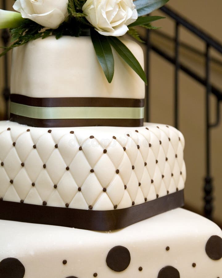 Close up of tiered white rolled fondant wedding cake, layers wrapped with brown and green ribbon decorated with quilted pattern and polka dots and topped with fresh white roses. Close up of tiered white rolled fondant wedding cake, layers wrapped with brown and green ribbon decorated with quilted pattern and polka dots and topped with fresh white roses