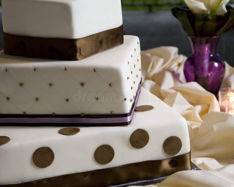 Close up of tiered white rolled fondant wedding cake, layers wrapped with brown and lavender ribbon decorated with quilted pattern and polka dots. Close up of tiered white rolled fondant wedding cake, layers wrapped with brown and lavender ribbon decorated with quilted pattern and polka dots