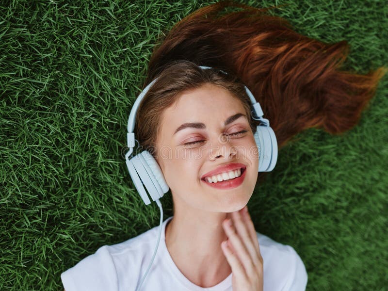 A woman lying on the green grass in spring with headphones on and her eyes closed listening to music. A woman lying on the green grass in spring with headphones on and her eyes closed listening to music