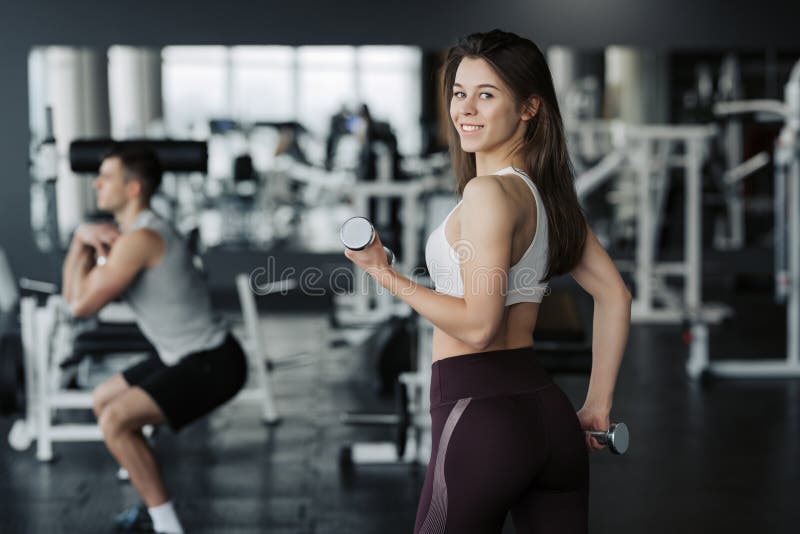 Весы молодой спортсменки поднимаясь в sportswear спортзала нося с ее парнем на предпосылке стоковые фото Весы молодой спортсменки поднимаясь в sportswear спортзала нося с ее парнем на предпосылке стоковые фото