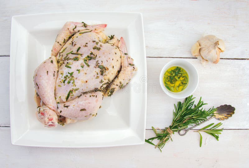 Whole chicken with oil, garlic and bunch of rosemary, preparation for grill roasting on white wooden table. Whole chicken with oil, garlic and bunch of rosemary, preparation for grill roasting on white wooden table