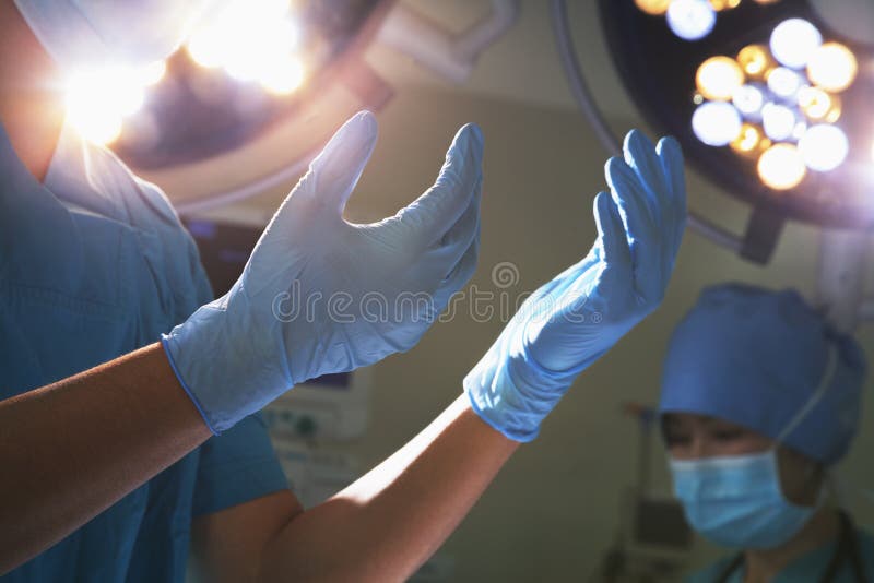 Midsection view of hands in surgical gloves and surgical lights in the operating room. Midsection view of hands in surgical gloves and surgical lights in the operating room