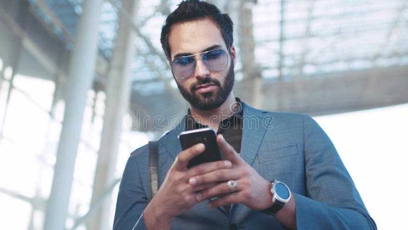 Взгляд вращения бородатого успешного человека используя его телефон входом авиапорта, сползающ экран, смотря вокруг