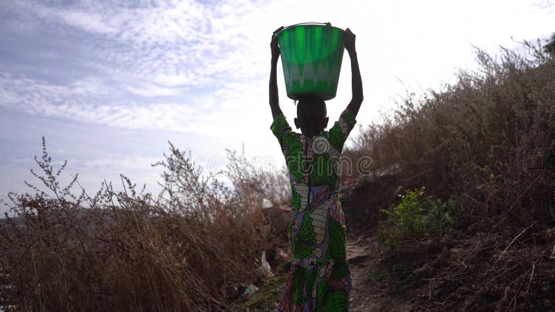 Взгляд назад молодой африканской девушки с домой ведро тяжелой воды из далекого места воды деревни
