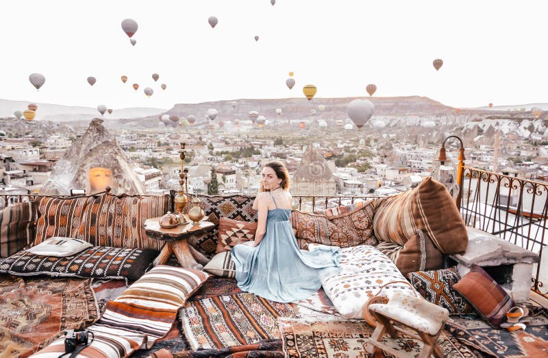 Взгляд утра в Cappadocia Взгляд террасы в женщине Goreme с горячими воздушными шарами и коврами стоковое изображение Взгляд утра в Cappadocia Взгляд террасы в женщине Goreme с горячими воздушными шарами и коврами стоковое изображение