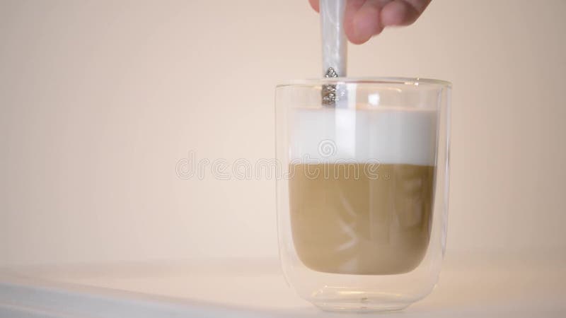 Взорвать руки женщины шевеля свежий кофе macchiato латте ложкой в чистой стеклянной кубке. видеоматериал