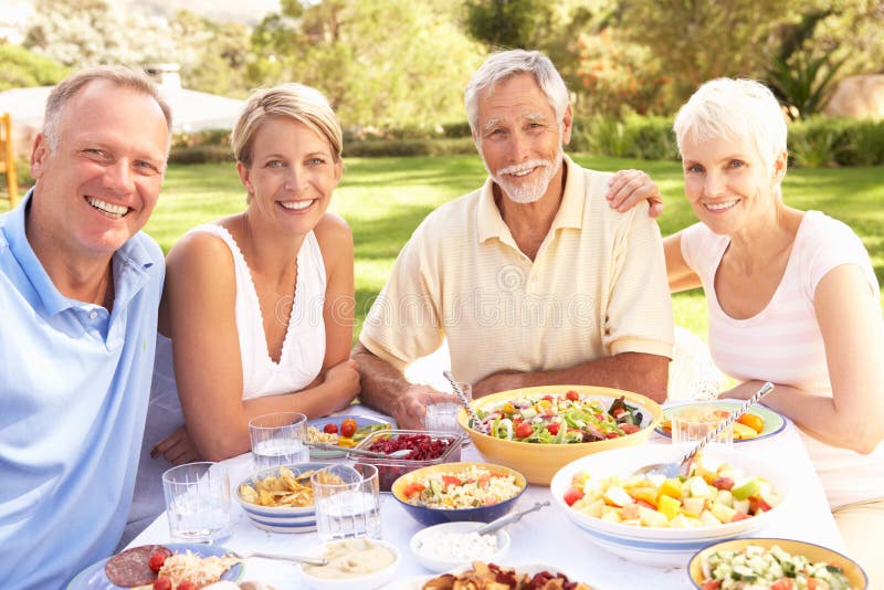 Adult Son And Daughter Enjoying Meal In Garden With Senior Parents. Adult Son And Daughter Enjoying Meal In Garden With Senior Parents