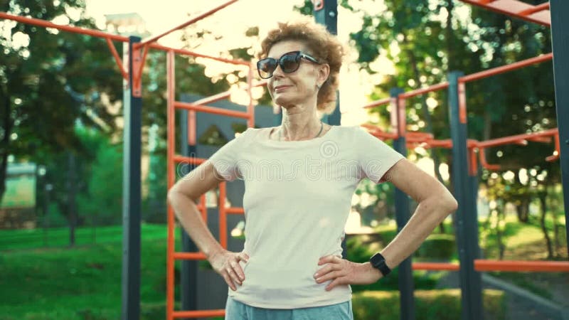 взрослая женщина разогревается перед тренировкой в спортзале летом. престарелые женщины проводят занятия по разогрев оружия и сток-видео