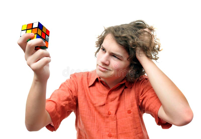 A young teenage adult problem solves with a puzzle cube isolated on white background while scratching his head in confusion. A young teenage adult problem solves with a puzzle cube isolated on white background while scratching his head in confusion.