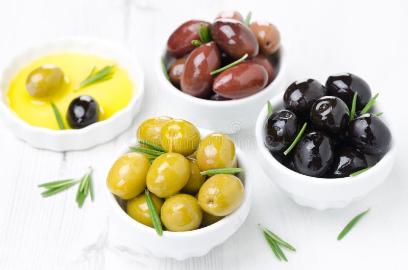 Three kinds of olives in bowls, fresh rosemary and olive oil on a white background, horizontal. Three kinds of olives in bowls, fresh rosemary and olive oil on a white background, horizontal