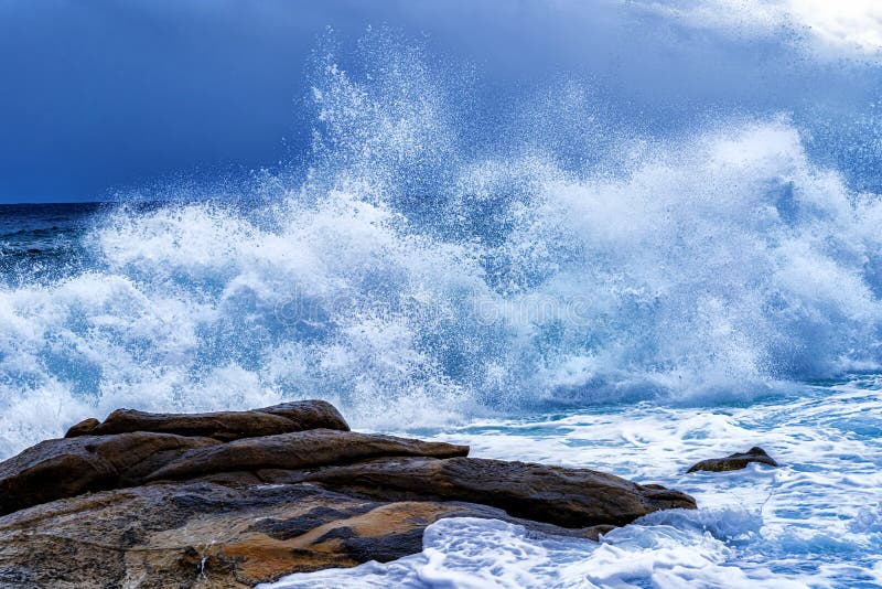 View of a huge storm at sea, with five meters high white splashing waves a threatening dark sky on the Mediterranean Sea in the summer, large colored boulders. on the front. View of a huge storm at sea, with five meters high white splashing waves a threatening dark sky on the Mediterranean Sea in the summer, large colored boulders. on the front