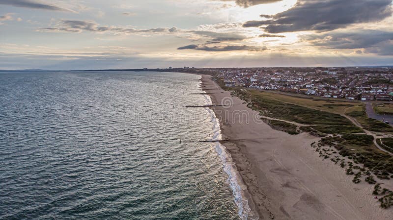 Вид с воздуха моря песчаного пляжа и открытого моря с городским районом морского побережья на заднем плане на заходе солнца с луч стоковое изображение Вид с воздуха моря песчаного пляжа и открытого моря с городским районом морского побережья на заднем плане на заходе солнца с луч стоковое изображение