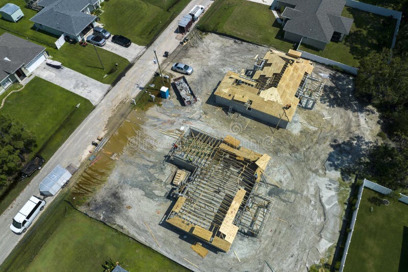 Aerial view of builders working on unfinished residential house with wooden roof frame structure under construction in Florida suburban area. Aerial view of builders working on unfinished residential house with wooden roof frame structure under construction in Florida suburban area.