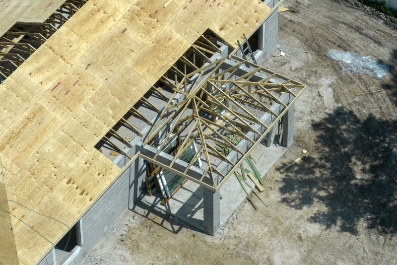 Aerial view of builders working on unfinished residential house with wooden roof frame structure under construction in Florida suburban area. Aerial view of builders working on unfinished residential house with wooden roof frame structure under construction in Florida suburban area.