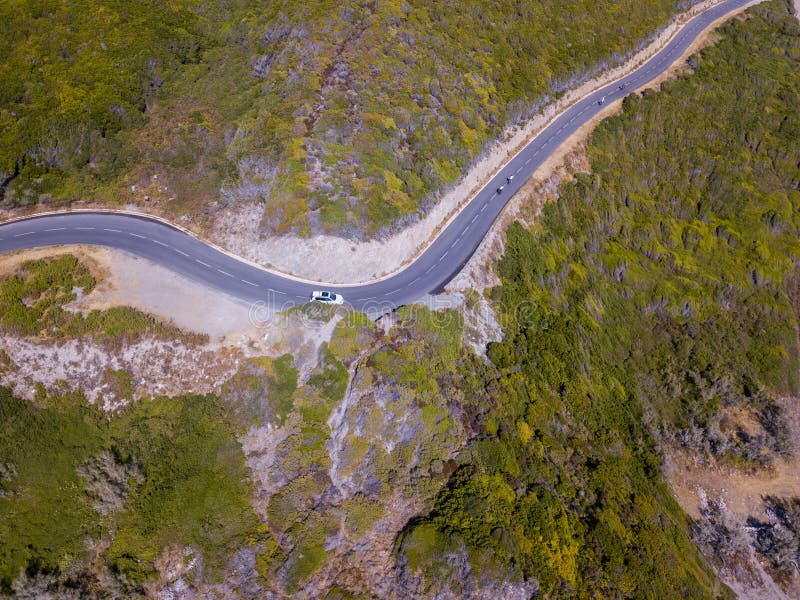 Aerial view of the coast of Corsica, winding roads. Cyclists running on a road. Peninsula of Cap Corse, Corsica. Coast line. Gulf of Aliso. France. Aerial view of the coast of Corsica, winding roads. Cyclists running on a road. Peninsula of Cap Corse, Corsica. Coast line. Gulf of Aliso. France