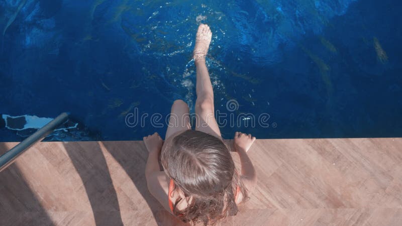 Вид сверху вниз на девушку, сидящую рядом с бассейном