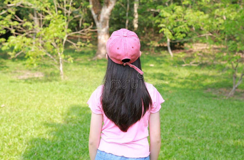 Вид сзади на молодую азиатскую девушку в кепке, которая стоит одна в саду стоковые фото