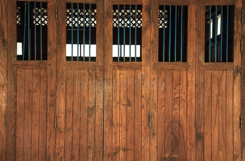 Vintage retro wooden doors and window panes with bars, home interior architectural design against plain tropical dark brown textured wood panel board wall in old Asian house. Vintage retro wooden doors and window panes with bars, home interior architectural design against plain tropical dark brown textured wood panel board wall in old Asian house