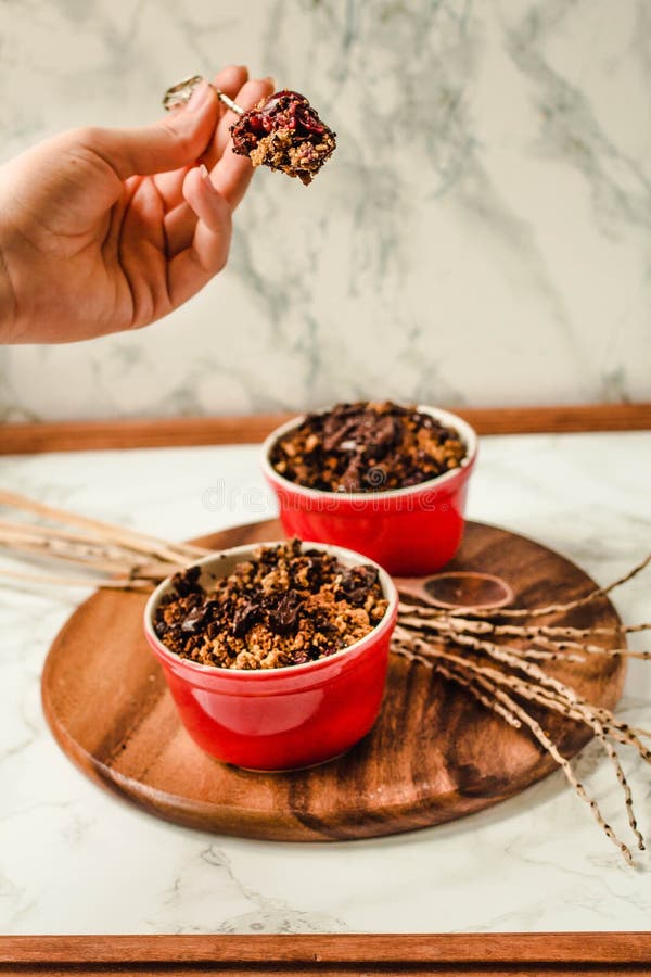 Вишня крошит с granola шоколада служила послуженный в разделанных красных плитах Процесс еды В руках молодой женщины стоковая фотография Вишня крошит с granola шоколада служила послуженный в разделанных красных плитах Процесс еды В руках молодой женщины стоковая фотография