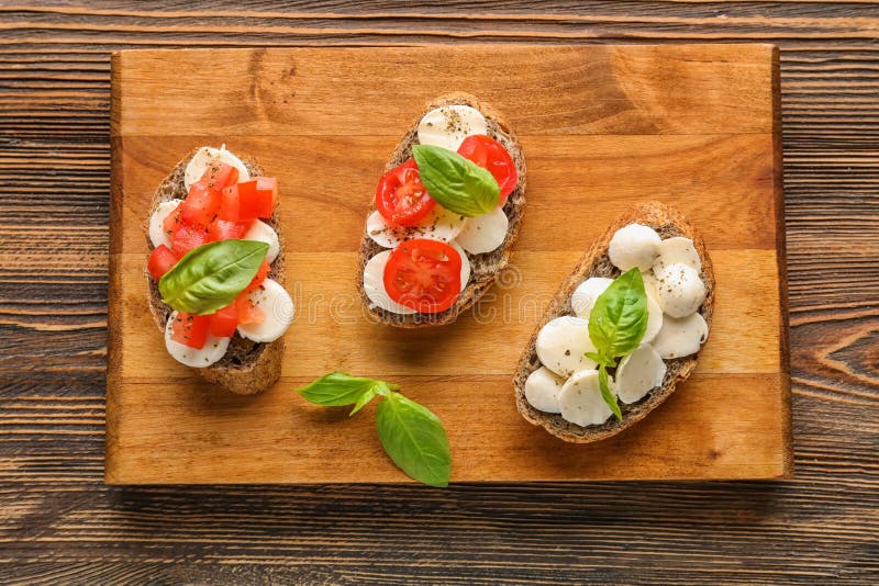 Вкусные сэндвичи с моццареллой, томатом и базиликом на деревянной доске стоковое изображение Вкусные сэндвичи с моццареллой, томатом и базиликом на деревянной доске стоковое изображение