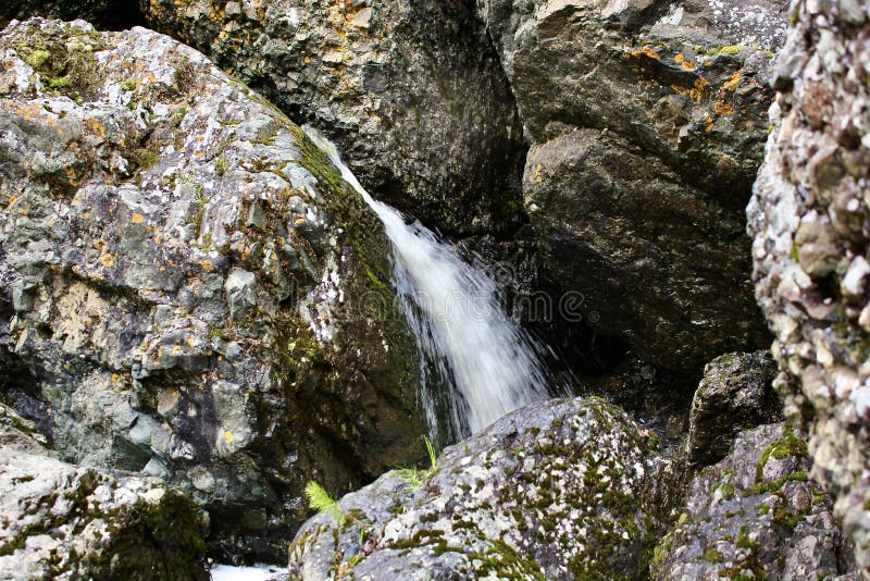 Водопад горной реки протекает через русло реки через огромные валуны с moss стоковое фото rf