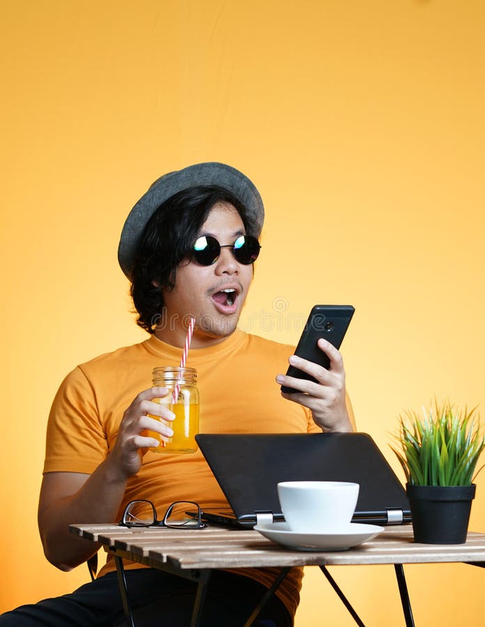 Возбужденный молодой человек сотрясенный и держащ Smartphone пока работающ o стоковые фото Возбужденный молодой человек сотрясенный и держащ Smartphone пока работающ o стоковые фото