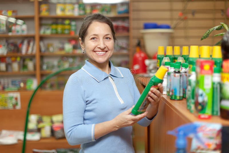 Smiling mature woman chooses fertilizers at store for gardeners. Smiling mature woman chooses fertilizers at store for gardeners