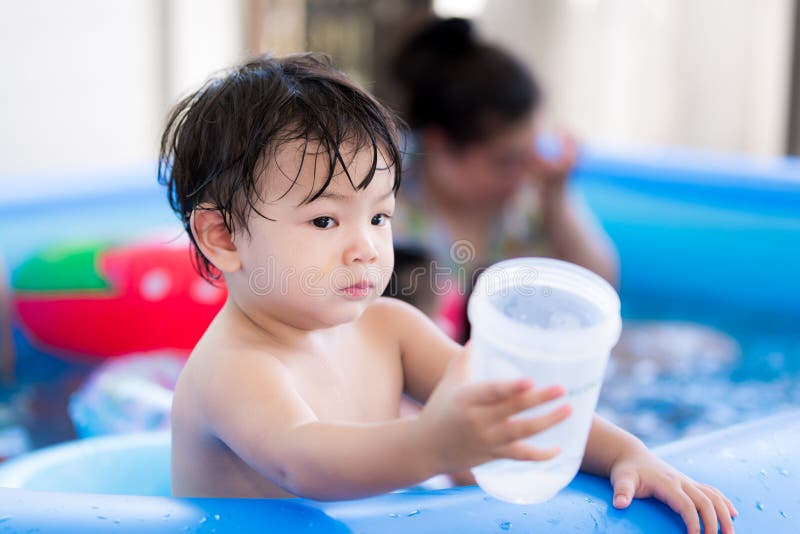 Boy age 1-2 year handed glass of water to someone and asked to add more water to plastic cup. Baby was thirsty after playing in water for long time. Child was thirsty. Children held in blue rubber pool. Boy age 1-2 year handed glass of water to someone and asked to add more water to plastic cup. Baby was thirsty after playing in water for long time. Child was thirsty. Children held in blue rubber pool.