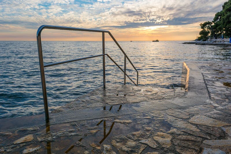 Восход солнца океана с пловцами металлические ограды ведущими в воду.