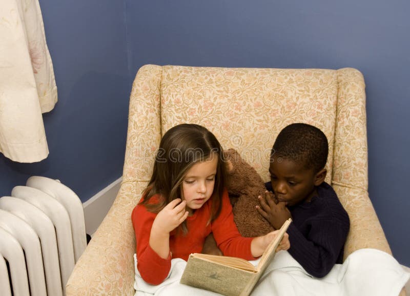 Two small children reading together in a big chair. Diversity. Two small children reading together in a big chair. Diversity.