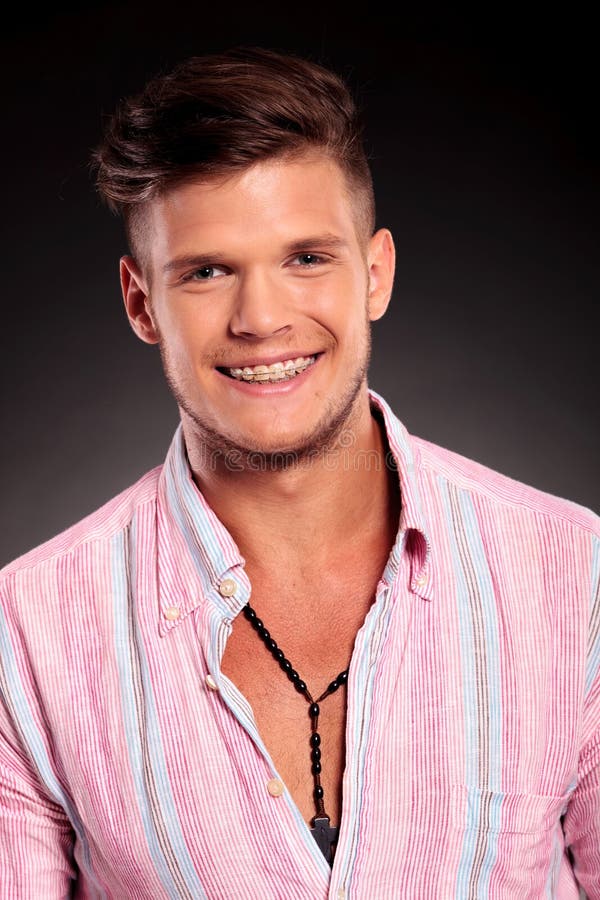 Beautiful young casual man smiling to the camera and revealing braces, on a light background. Beautiful young casual man smiling to the camera and revealing braces, on a light background