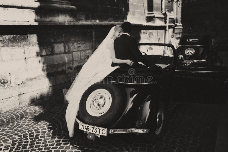 Вуаль невесты висит вниз пока она сидит с groom на ретро автомобиле стоковая фотография Вуаль невесты висит вниз пока она сидит с groom на ретро автомобиле стоковая фотография