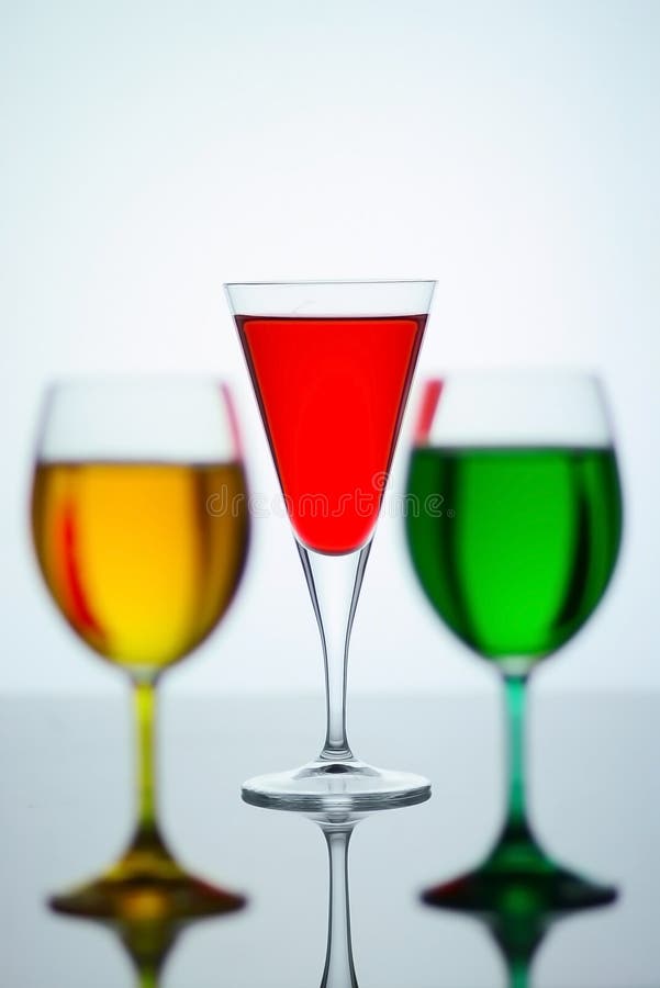 Select the focus of the glass in the middle of the back with 2 more glasses in the front with a different color of water. Select the focus of the glass in the middle of the back with 2 more glasses in the front with a different color of water