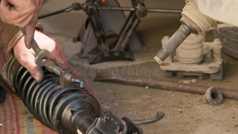 выбитые руки механика закручивают пружину катушки гаечным ключом во время ремонта автомобиля.