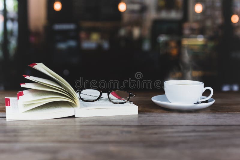 Выбранный фокус кофейной чашки с открытыми книгой и стеклами на woode стоковая фотография Выбранный фокус кофейной чашки с открытыми книгой и стеклами на woode стоковая фотография