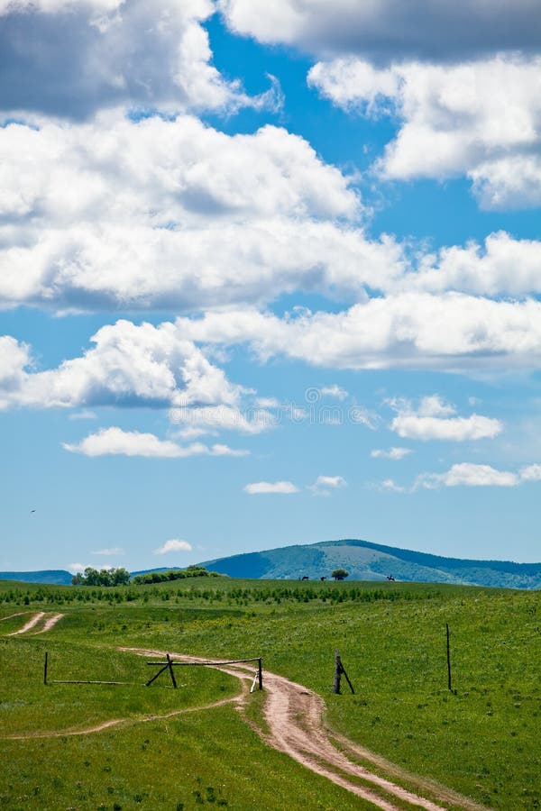 A path leading to the depths of grassland pastures with blue sky and white clouds. A path leading to the depths of grassland pastures with blue sky and white clouds.