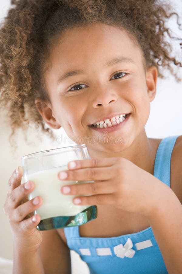 Young girl indoors drinking milk smiling at camera. Young girl indoors drinking milk smiling at camera