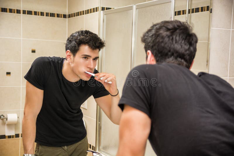 Headshot of attractive young man brushing teeth with toothbrush, looking at himself in mirror. Headshot of attractive young man brushing teeth with toothbrush, looking at himself in mirror