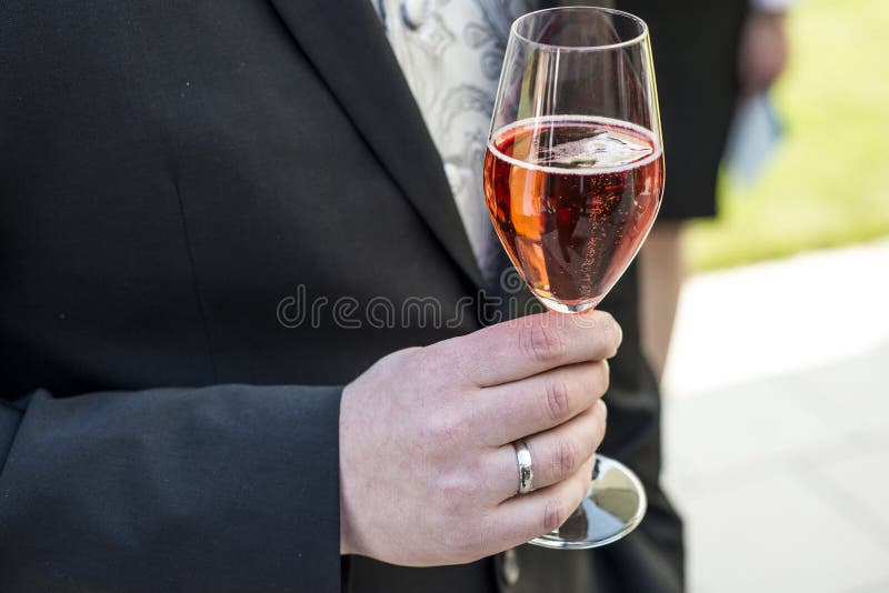 Выхольте держать стеклянное игристое вино wedding красное кольцо крупного плана костюма шампанского стоковое изображение rf Выхольте держать стеклянное игристое вино wedding красное кольцо крупного плана костюма шампанского стоковое изображение rf