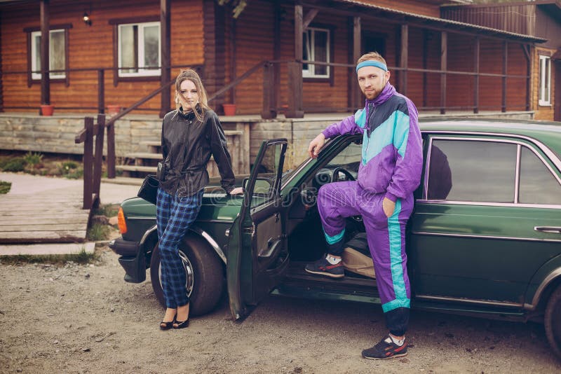 Гай и девушка в одеждах девяностых годов, рядом с старым автомобилем стоковое фото rf Гай и девушка в одеждах девяностых годов, рядом с старым автомобилем стоковое фото rf