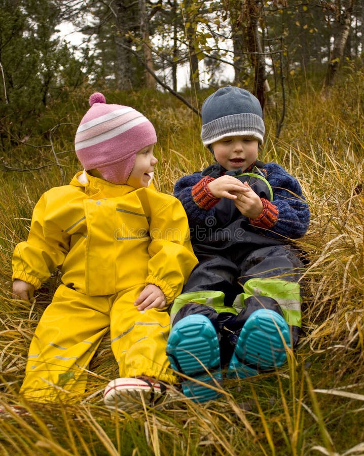 Two small children (2 and 3 years old) sitting outside in an autumn forest, talking. Two small children (2 and 3 years old) sitting outside in an autumn forest, talking.