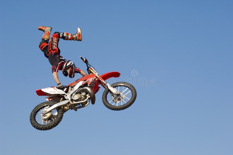 Гонщик Motocross выполняя эффектное выступление с мотоциклом в Midair против неба стоковая фотография Гонщик Motocross выполняя эффектное выступление с мотоциклом в Midair против неба стоковая фотография