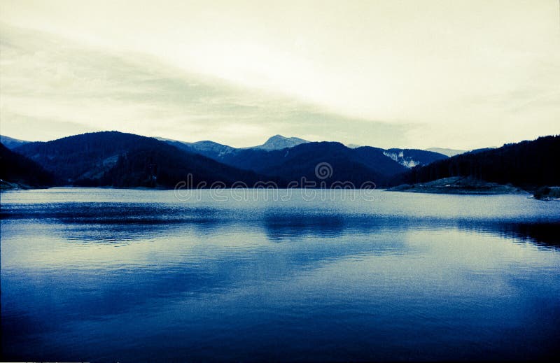 Calm mountain lake with forested hills and sky covered by clouds. Calm mountain lake with forested hills and sky covered by clouds