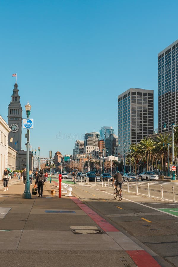 San Francisco, California, April 8, 2024. Urban street scene at The Embarcadero with cyclists and pedestrians, flanked by high-rise buildings and palm trees. San Francisco, California, April 8, 2024. Urban street scene at The Embarcadero with cyclists and pedestrians, flanked by high-rise buildings and palm trees