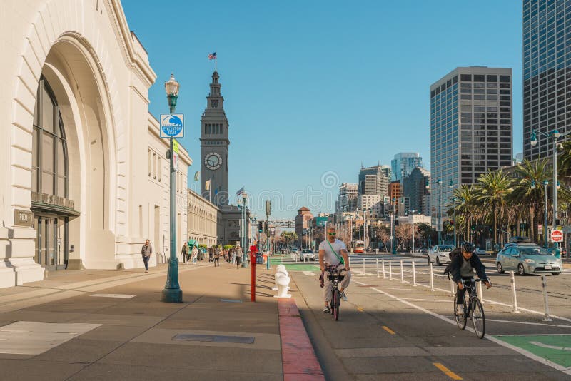 San Francisco, California, April 8, 2024. Urban street scene at The Embarcadero with cyclists and pedestrians, flanked by high-rise buildings and palm trees. San Francisco, California, April 8, 2024. Urban street scene at The Embarcadero with cyclists and pedestrians, flanked by high-rise buildings and palm trees