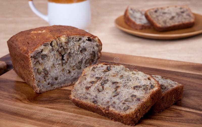 Sliced loaf of banana walnut bread on a cutting board with one serving of two slices and a mug in the background. Sliced loaf of banana walnut bread on a cutting board with one serving of two slices and a mug in the background