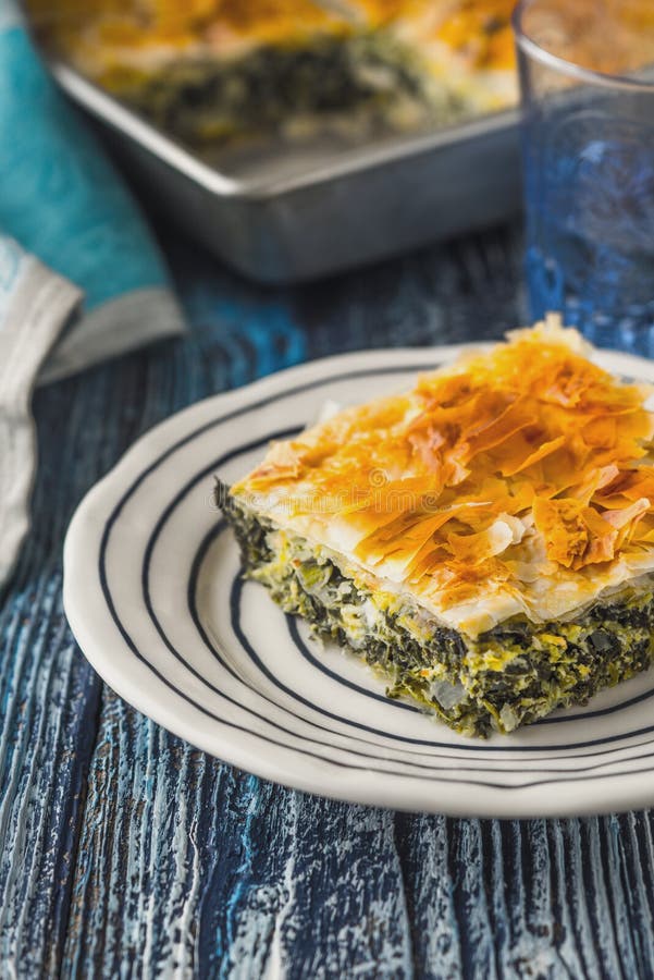 Греческое spanakopita пирога в белой плите на голубом деревянном столе стоковые изображения rf Греческое spanakopita пирога в белой плите на голубом деревянном столе стоковые изображения rf