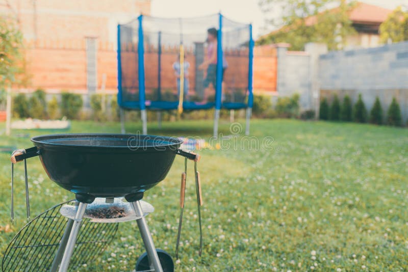 Гриль барбекю BBQ угля чайника в саде или задворк Запачканный на открытом воздухе батут на заднем плане Родной дом стоковое изображение rf Гриль барбекю BBQ угля чайника в саде или задворк Запачканный на открытом воздухе батут на заднем плане Родной дом стоковое изображение rf