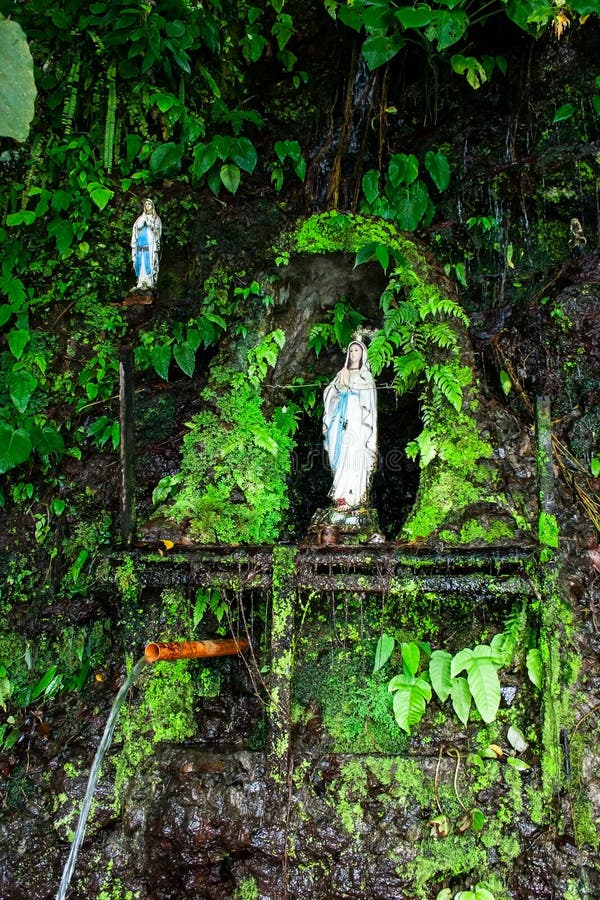 Two virgin Mary statues surrounded by lush tropical vegetation such as sterns with a with fresh water pipe on a cliff falling into Pandin lake,  one of the seven lakes of San Pablo, Laguna Province, Luzon island, Philippines. Two virgin Mary statues surrounded by lush tropical vegetation such as sterns with a with fresh water pipe on a cliff falling into Pandin lake,  one of the seven lakes of San Pablo, Laguna Province, Luzon island, Philippines